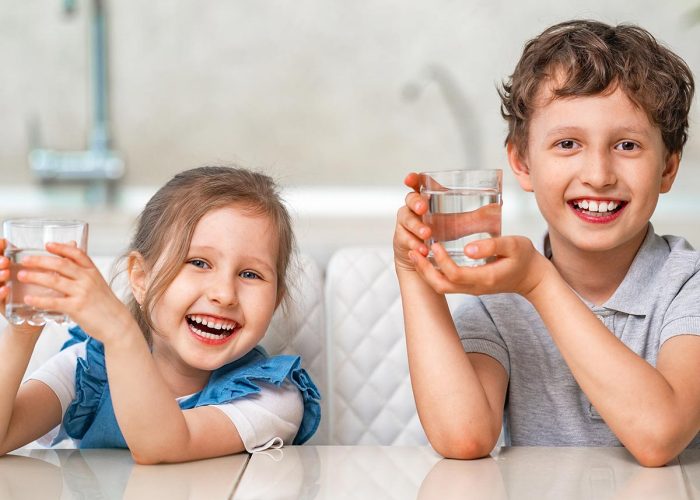 Funny little children drink water in the kitchen at home.